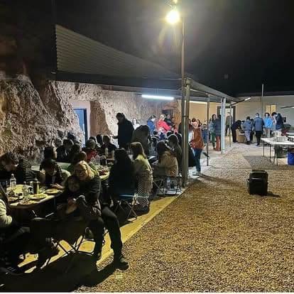 A communal trestle-table dinner under a lit awning at a multi-day tour venue.